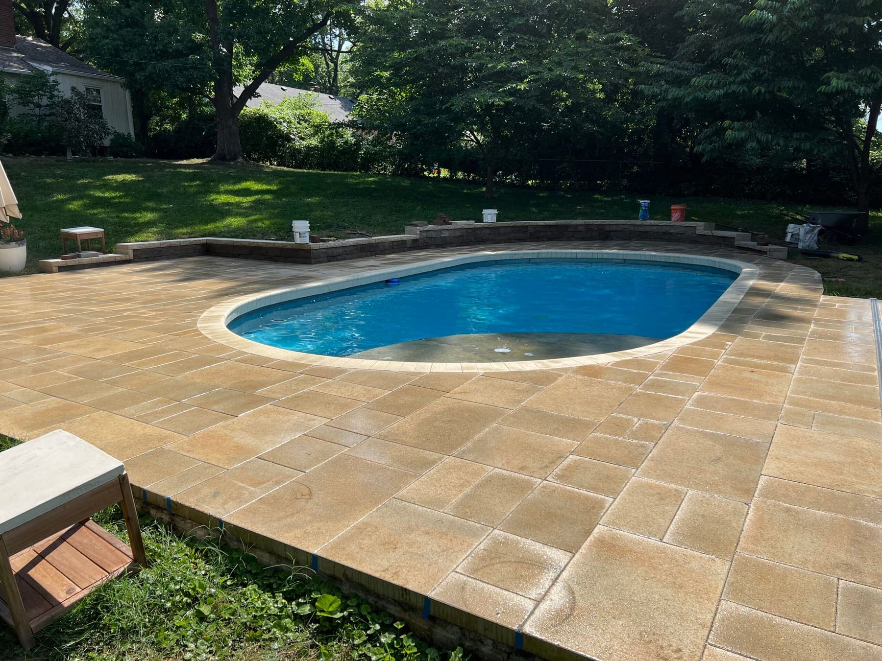 Paver patio surrounding an oval swimming pool with a low retaining wall